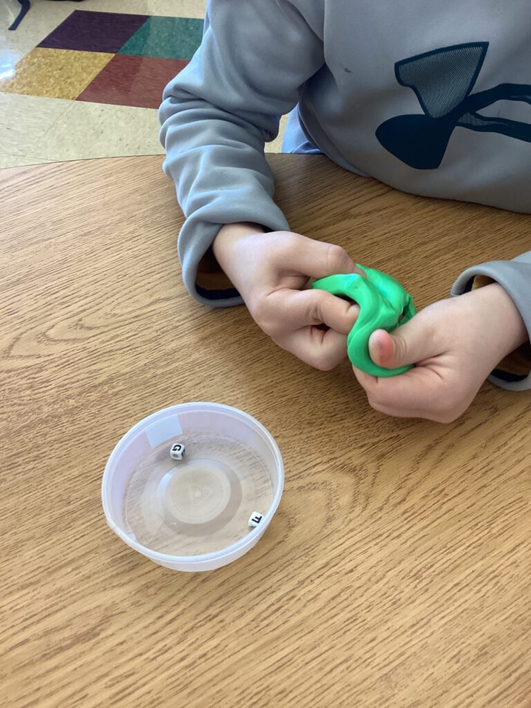 student using green theraputty to find hidden letter beads