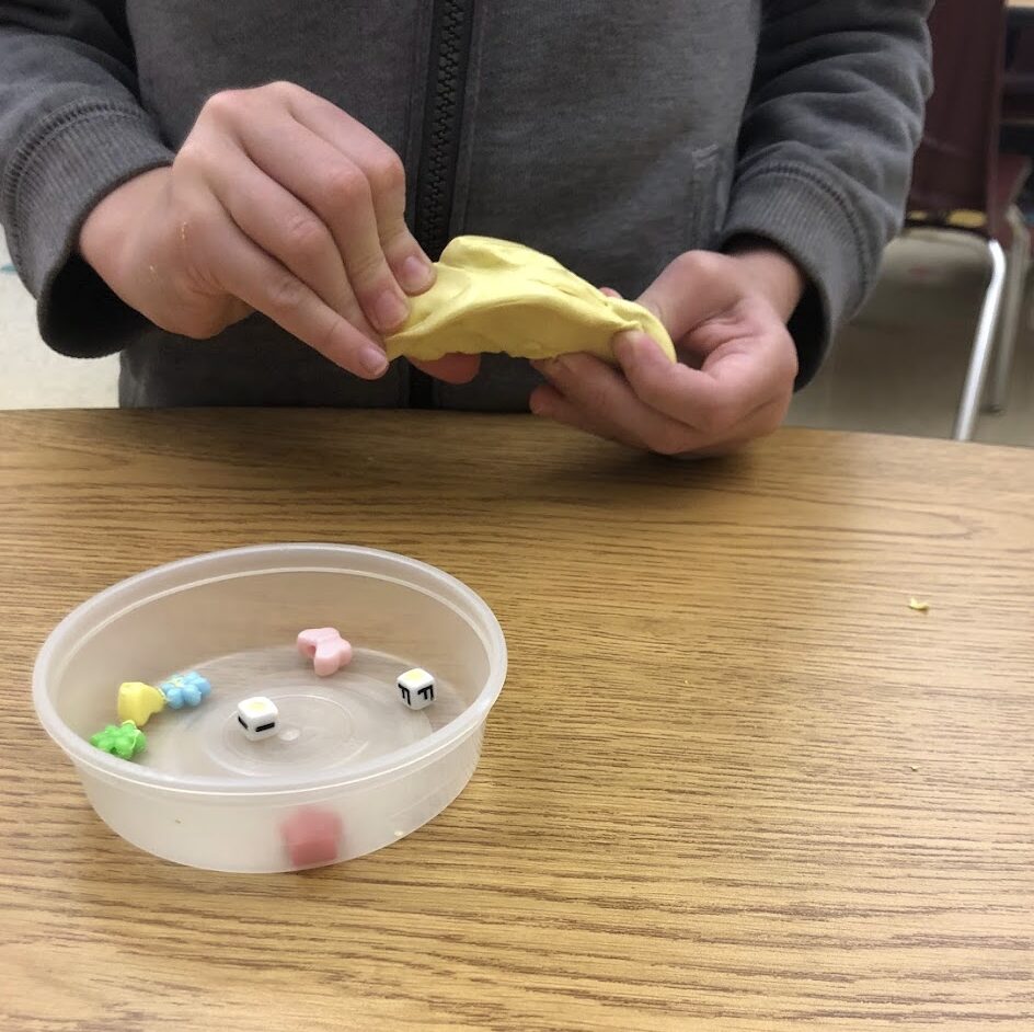 child stretching yellow theraputty to get alphabet beads and other shapes hidden within it