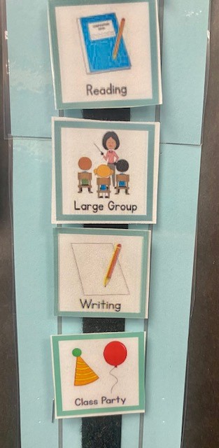 A blue schedule board with schedule pieces that show reading, large group, writing, and class party.