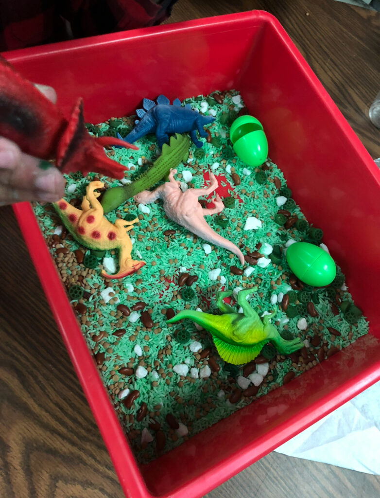 spring sensory bin with green dyed rice, beans, plastic eggs and dinosaur toys