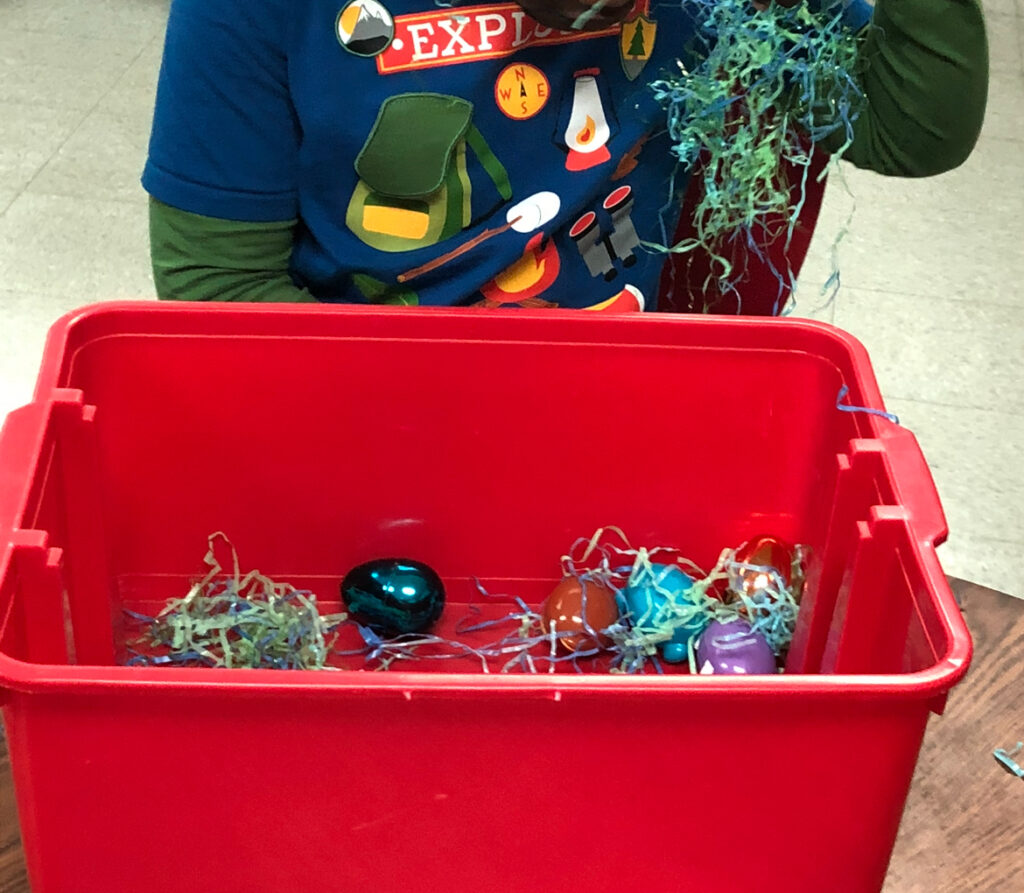 red bin with Easter grass and Easter eggs being used by a student as a sensory bin