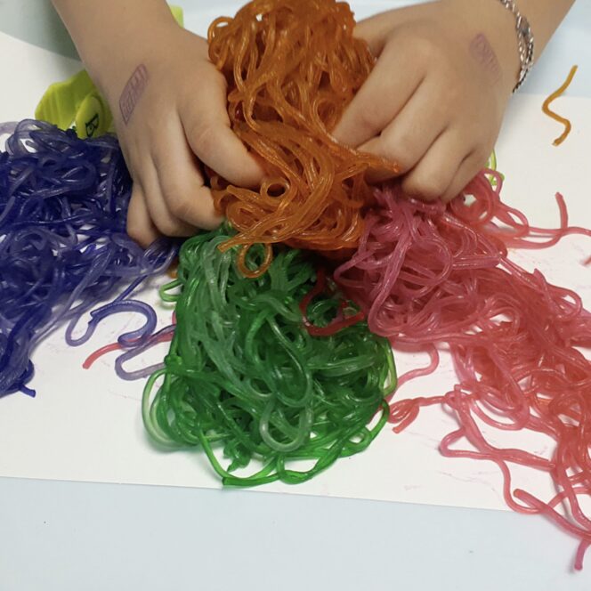 spaghetti noodles dyed purple, orange, pink and green for a sensory bin and a student playing with it