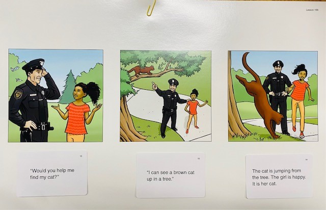 A white board with a series of three pictures showing a girl speaking to a police officer about a cat stuck in a tree. Under each picture is a card with a matching caption.