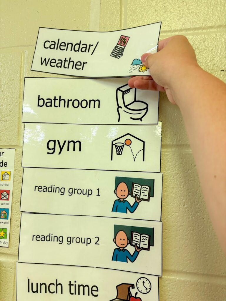 hand pulling off the first schedule piece from the top of a classroom schedule