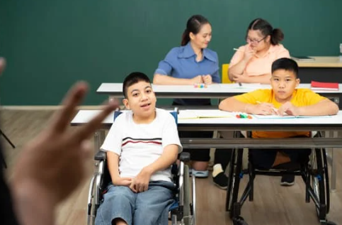 Three students and a teacher are shown sitting at desks in a classroom