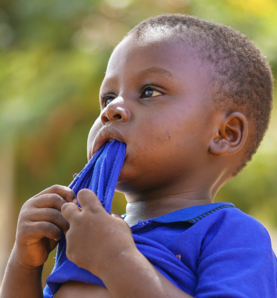 child chewing on the bottom hem of their blue shirt