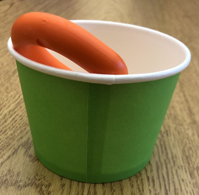 orange oral sensory seeking tool in a small green cup for storage when not in use