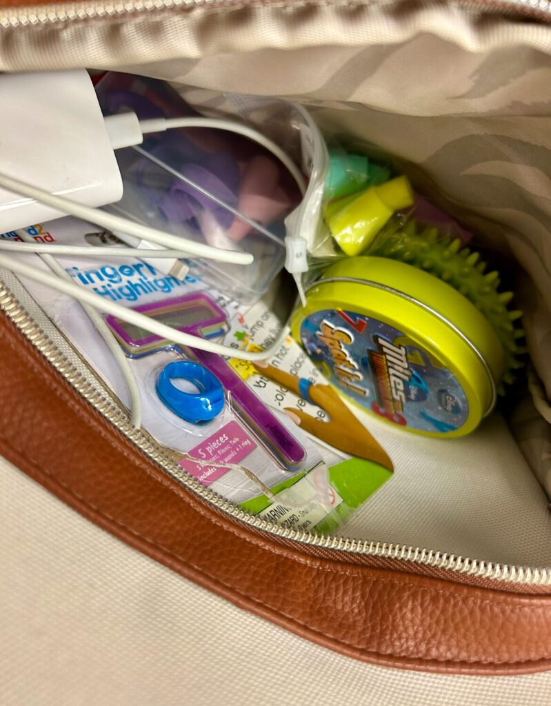 the inside of the front pocket of my OT bag that includes a charger, finger follow highlighter tool, Spot It game, pencil grips and a sensory fidget