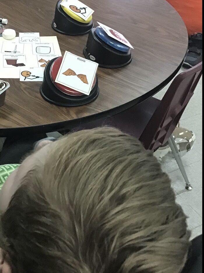 student sitting at a table with core vocabulary words on switches [more, eat, etc.]