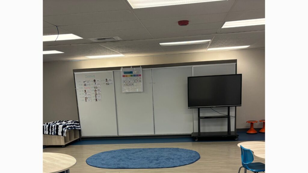 Image of a classroom with a blue rug, calendar, visual schedule, and Smart Board.