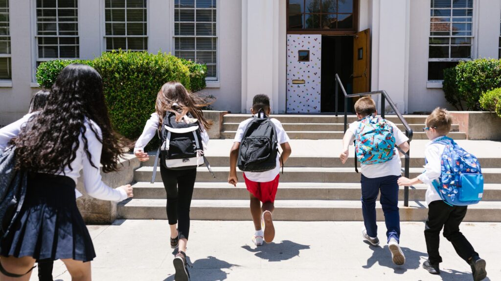 children with backpacks head up stairs and into a school building