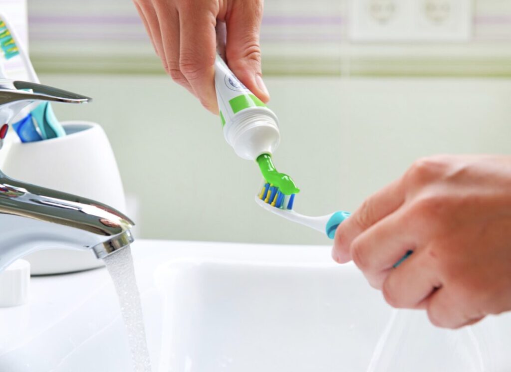 person putting toothpaste on a toothbrush