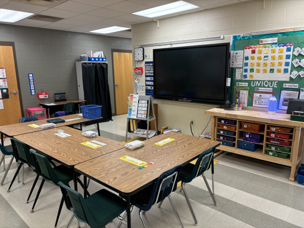 a middle school classroom with student tables, touchscreen board, calendar, and visuals