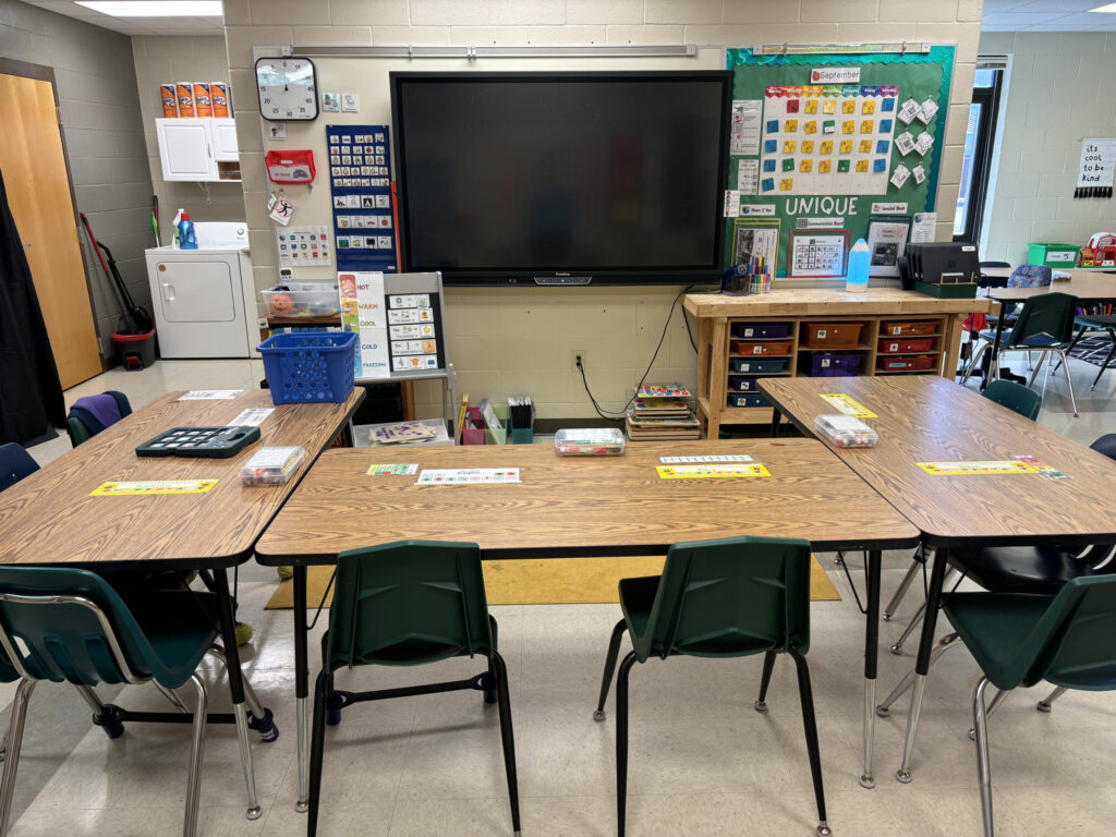 Three tables are placed together in front of a board for students to sit together in whole group