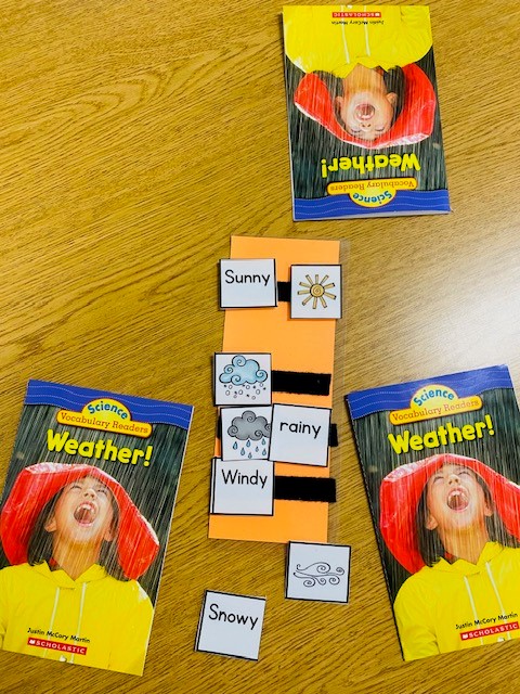 On a wooden table, there are several readers titled "Weather!" and a a weather vocabulary matching activity.