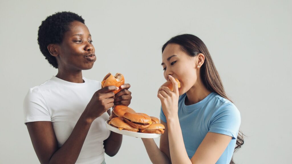 two teenage girls eat a plate of hamburgers