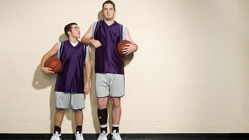 two students play basketball, one is much taller than the other