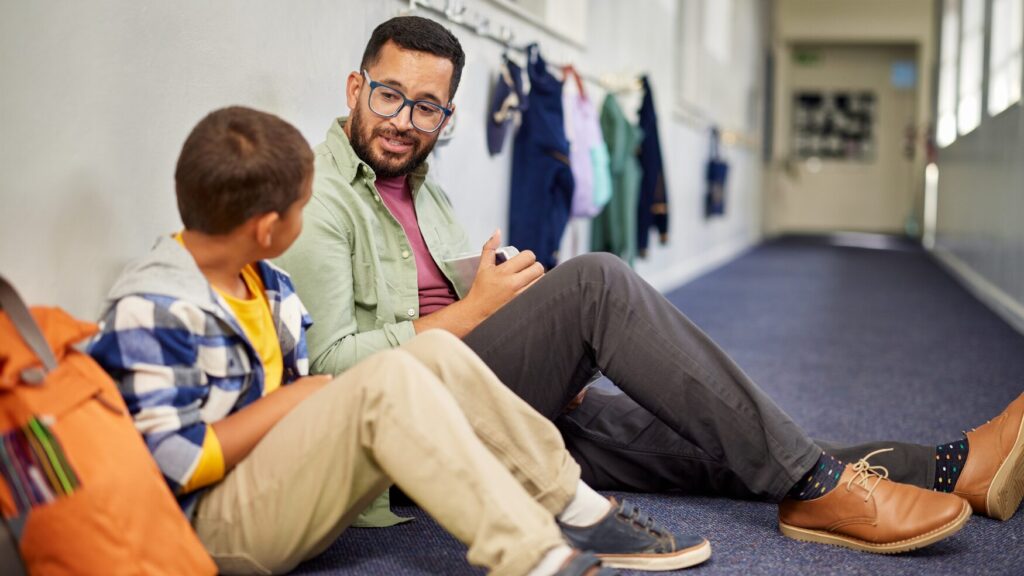 a teacher sits on a hallway floor with a student
