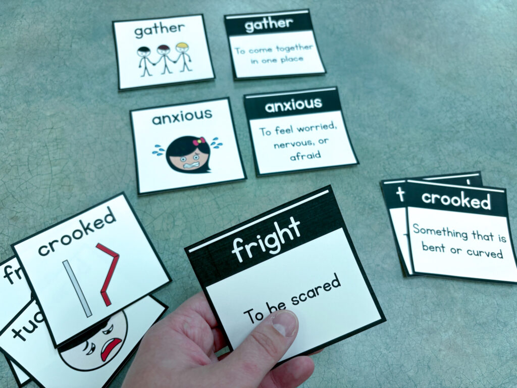 Vocabulary cards with visual symbols and without sit on a table. A hand holds one card.