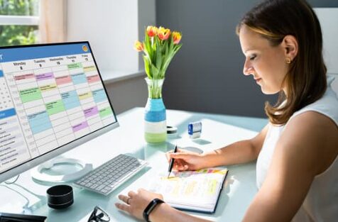 A woman sits in front of a computer, working on a scheduling chart.