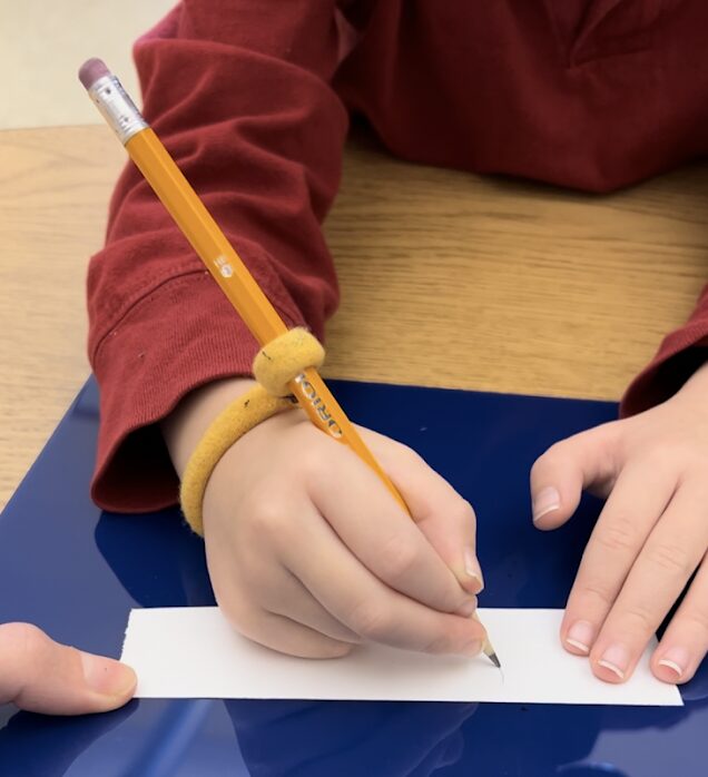 Student using a blue slant board and handiwriter pencil grip