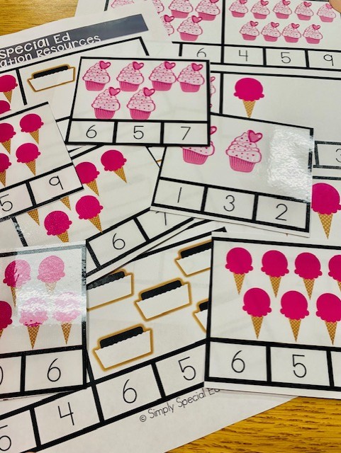 A group of colorful counting clip cards are shown. The cards have images of ice cream, cupcakes, and other treats. Each card has a certain number of items on it, with digit choices underneath,