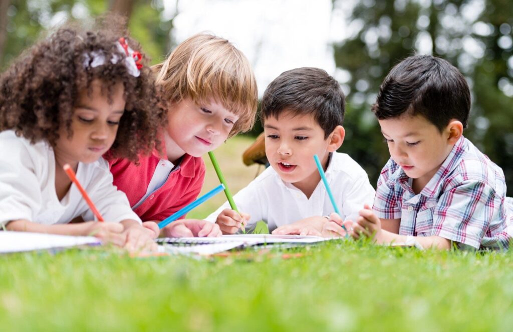 children sitting in the grass writing in notebooks