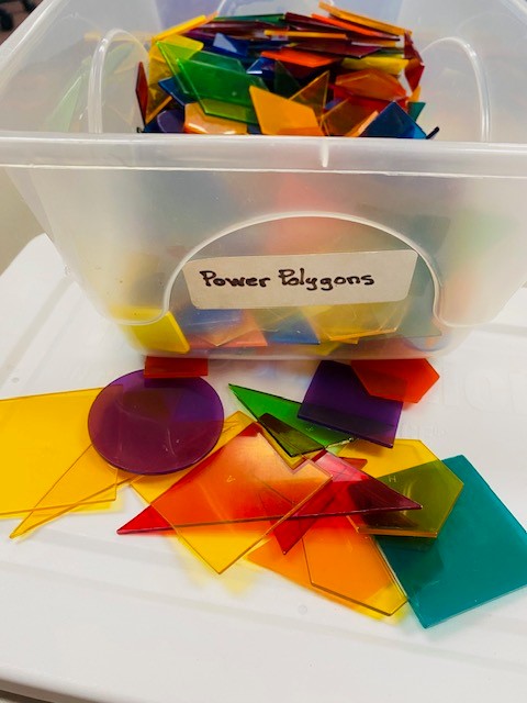 A clear plastic bin labeled "Power Polygons" is filled with colorful plastic shapes.