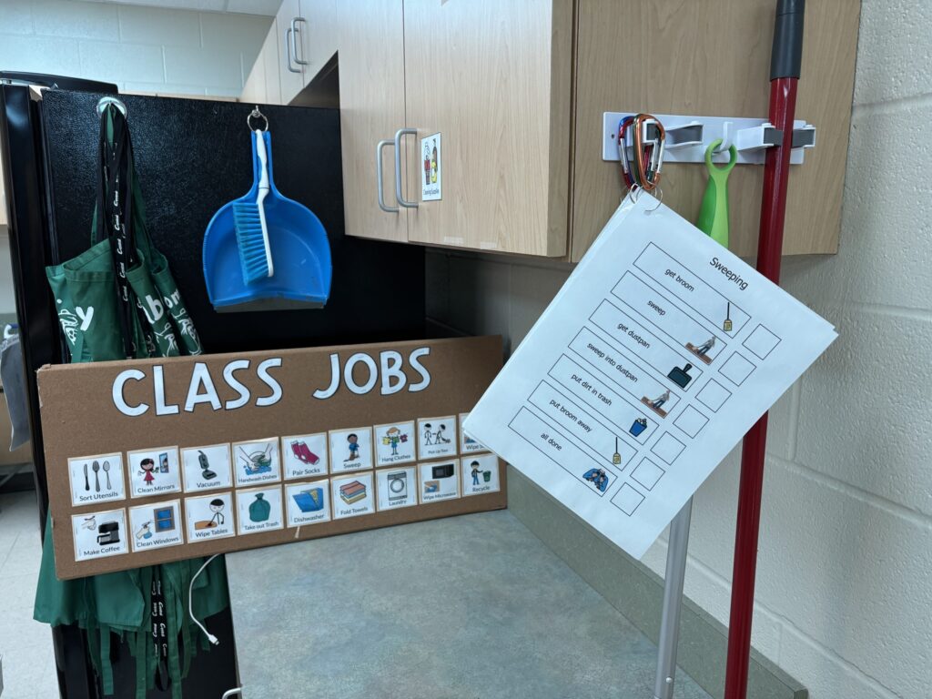a classroom jobs board provides choices for custodial related vocational tasks. A task analysis hangs with visuals for sweeping.