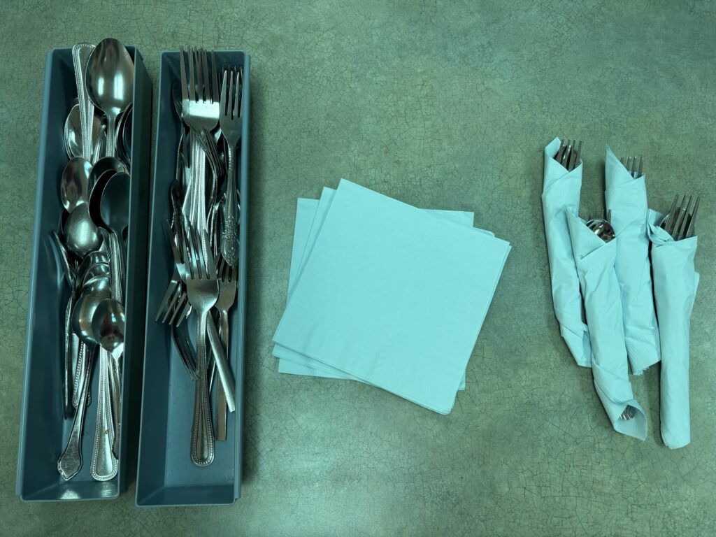 spoons, forks, and napkins are set out for a student to practice wrapping a set of utensils