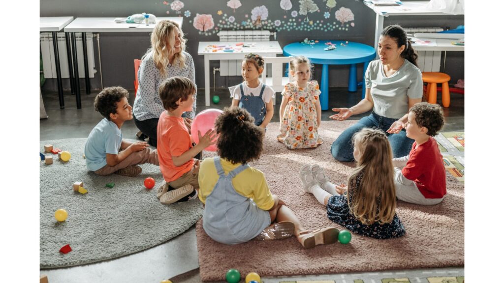 Image with two adults and seven children sitting around in a circle, engaging in an activity involving a ball.