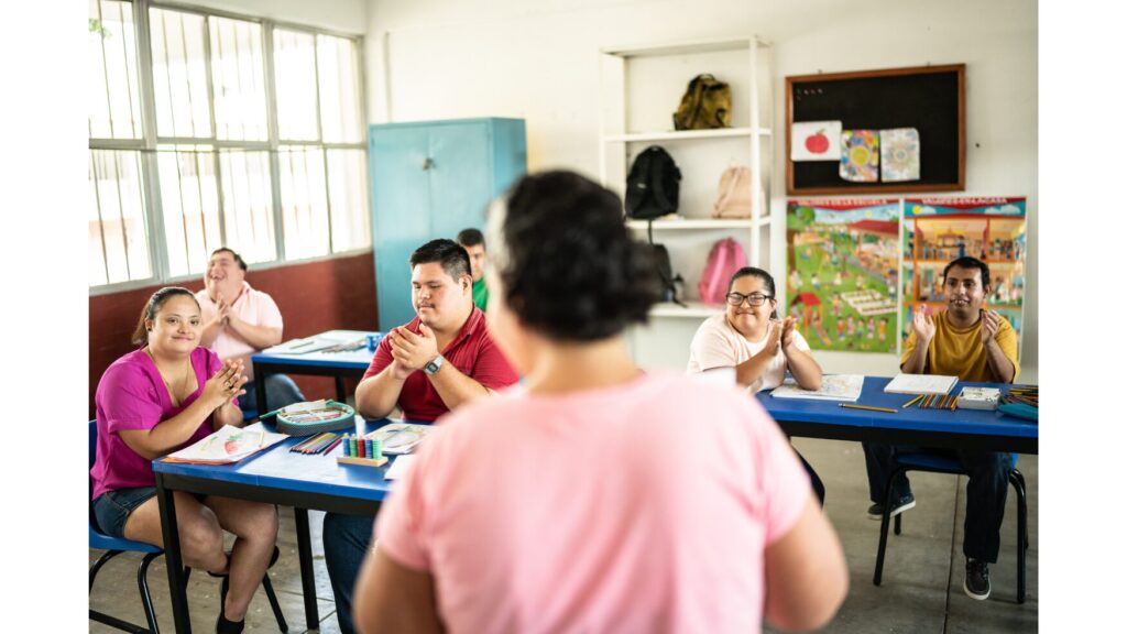 Image of a classroom with six students with disabilities. In the front of the room is an individual facing the class.