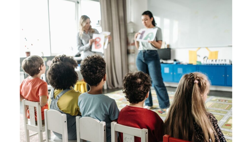 Image featuring two adults in front of 4 children. The adults are holding up papers with with letters "A" and "B" on them respectively.