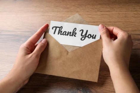 A pair of hands holding at hank you note in an envelope.