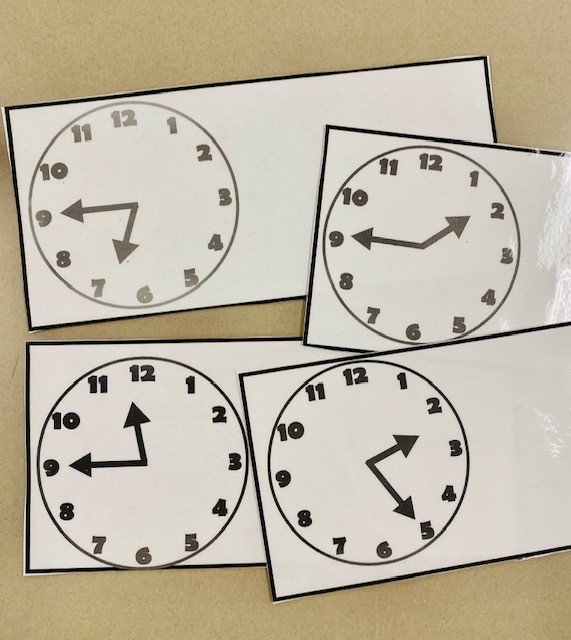 Four laminated task cards with different analog clocks on the.
