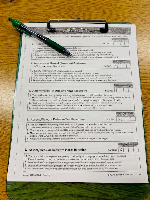 A page of the VB-MAPP assessment is shown on a clipboard, with a green pen.