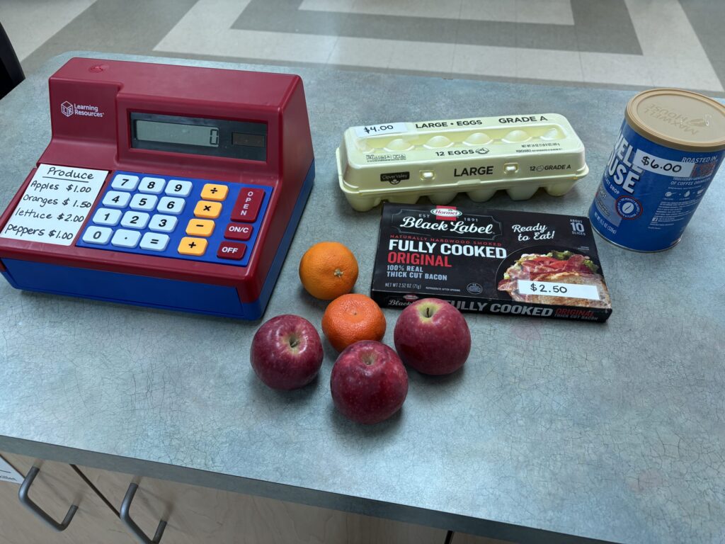 apples, oranges, eggs, bacon, and coffee are supplied near a cash register for students to practice vocational skills