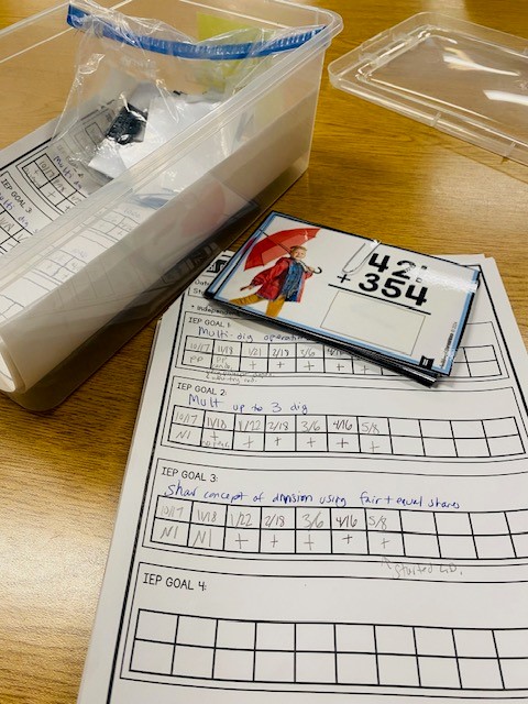 Goal data sheet is shown on a table. A plastic goal bin and task cards are also shown.