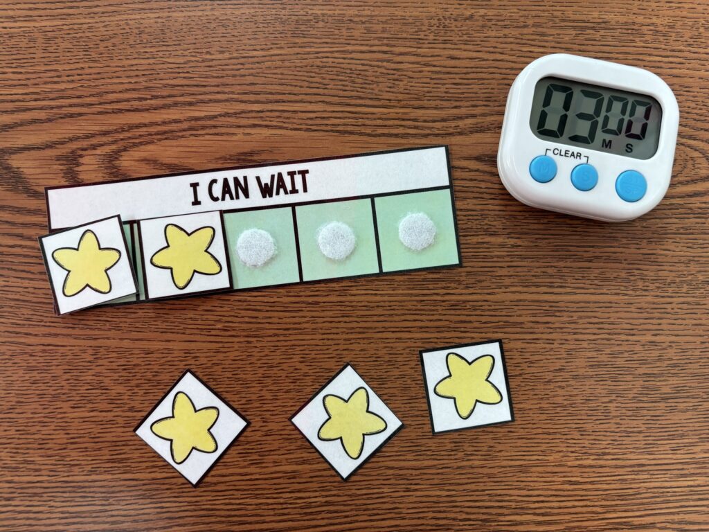 A token economy "I can wait" board with velcro stars sits next to a timer on a brown desktop
