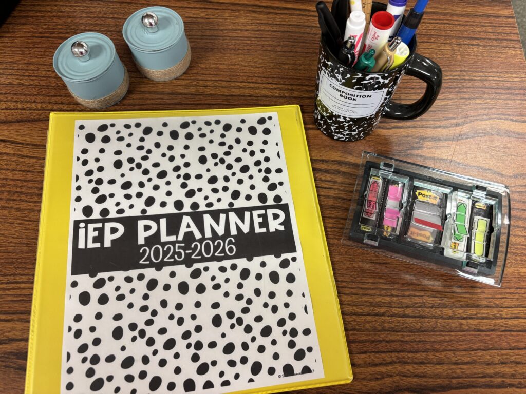 An IEP Binder sits on a desktop with sticky note flags, jars of paper clips, and a mug of pens.