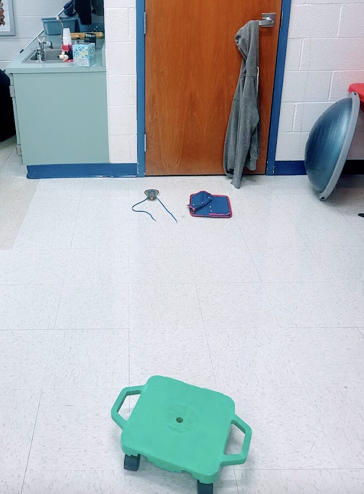 sweatshirt, shoe tying card and snap clothing fastener board across from a scooter board in the sensory room