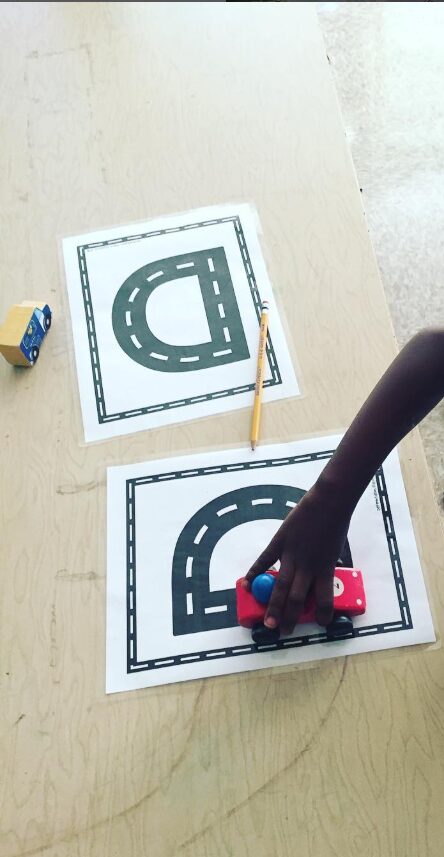 Child playing with a toy car to trace the letter D 