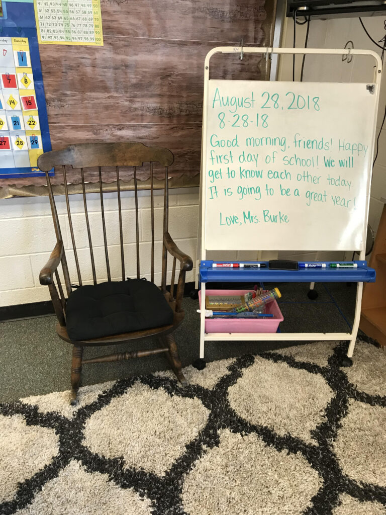 Easel in a classroom next to a rocking chair showing a morning greeting message