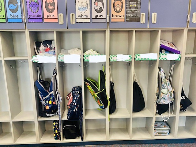 A row of cubbies in a classroom with nametags and backpacks.