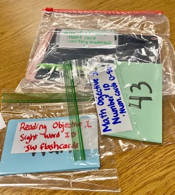 Plastic baggies with goal materials are on a table. Each baggie has a color-coded objective written on it.