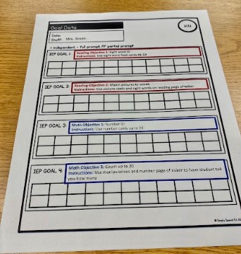 A printed goal data sheet is on a table. The goals are typed in red and blue.