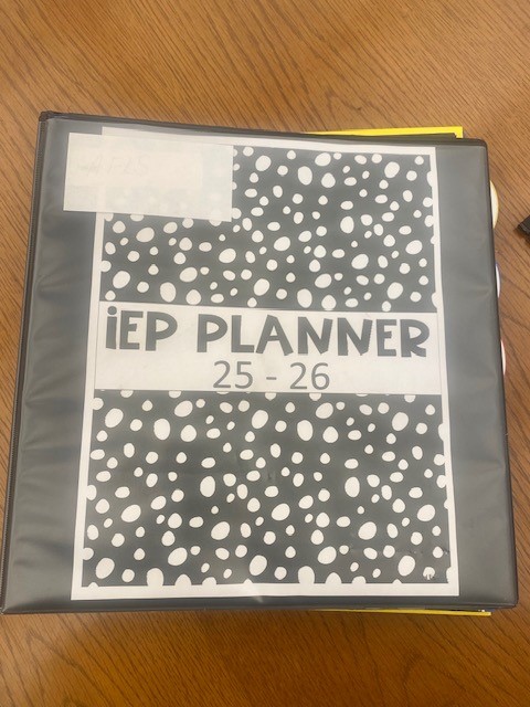 A binder is shown on a wooden table. The cover reads "IEP Planner 25-26"