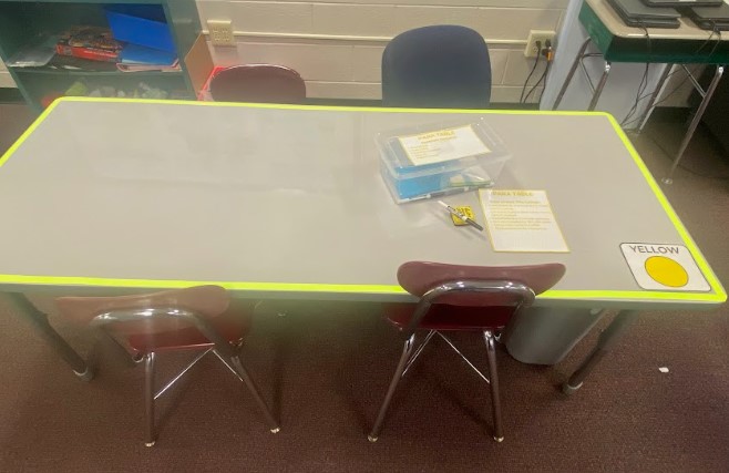 A white table with a yellow border is shown in a classroom