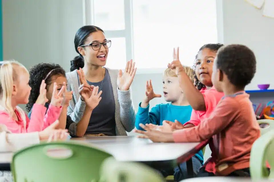 An educator working with a small group of students that are holding up their fingers 