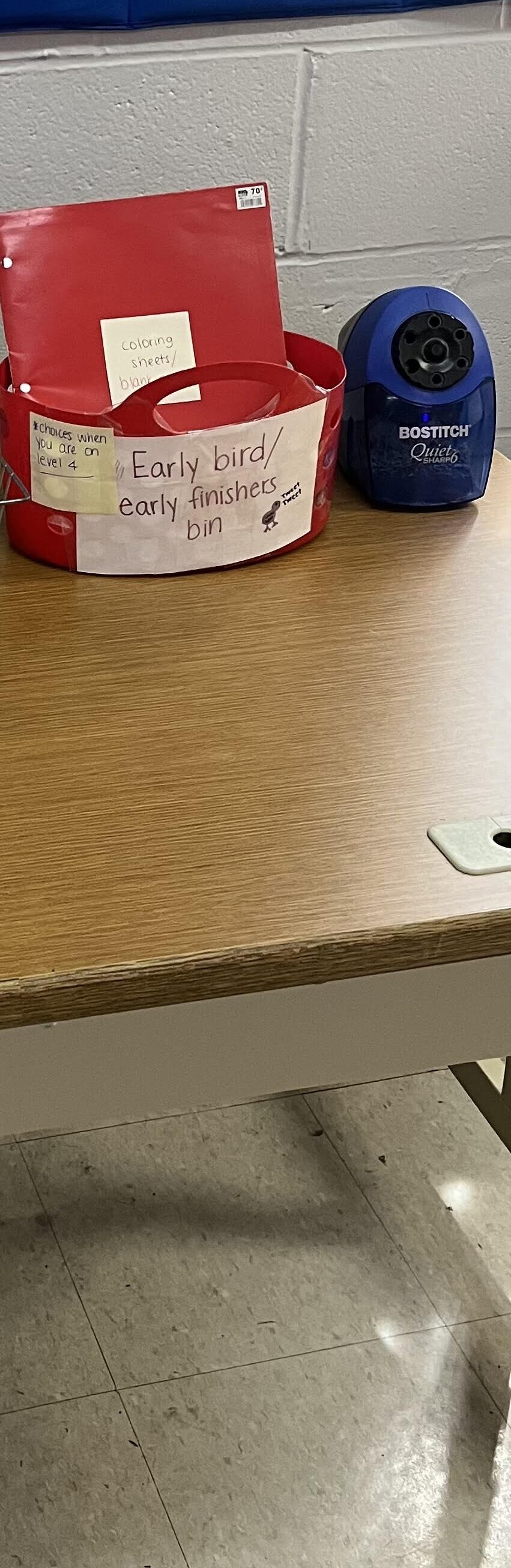 red bin with red folder in it next to blue pencil sharpener